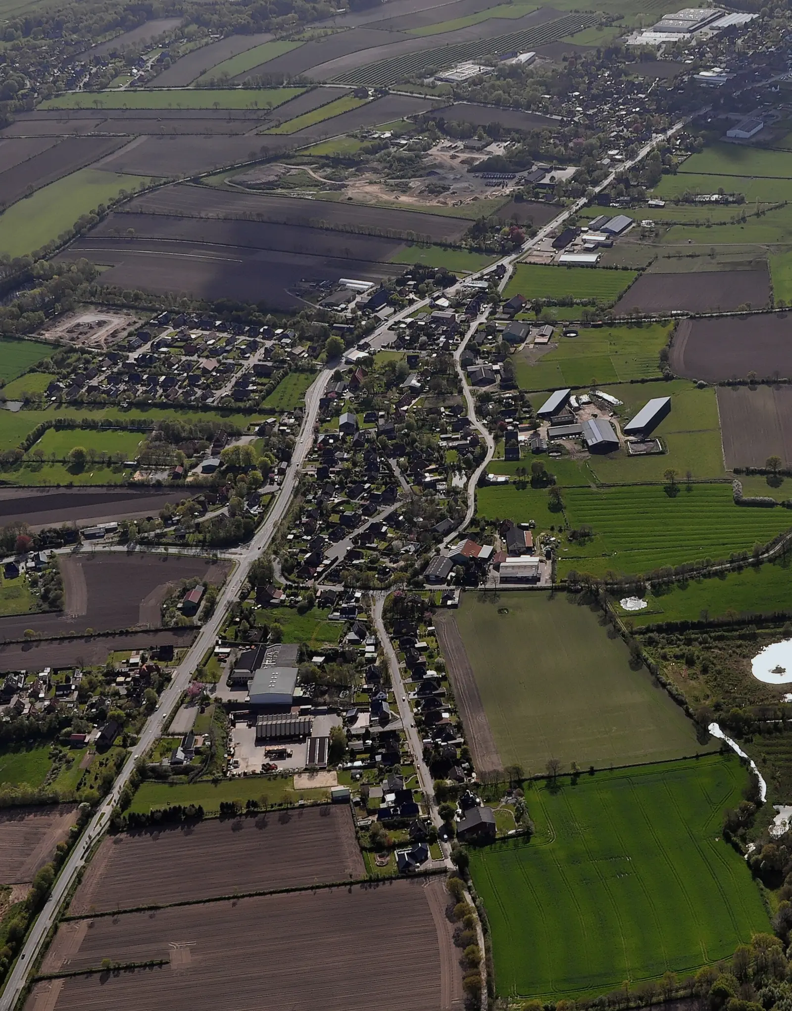 Nindorf von oben: die Hauptstraße zieht sich durch das Dorf, rundherum Felder und Weiden der Dithmarscher Geest